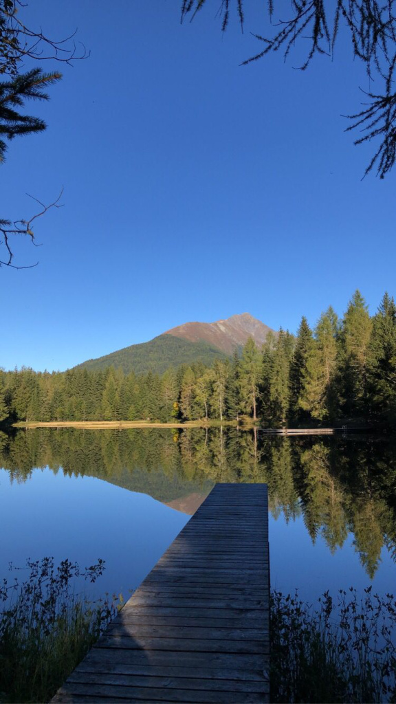 Holzsteg am See mit Berg und Wald im Hintergrund